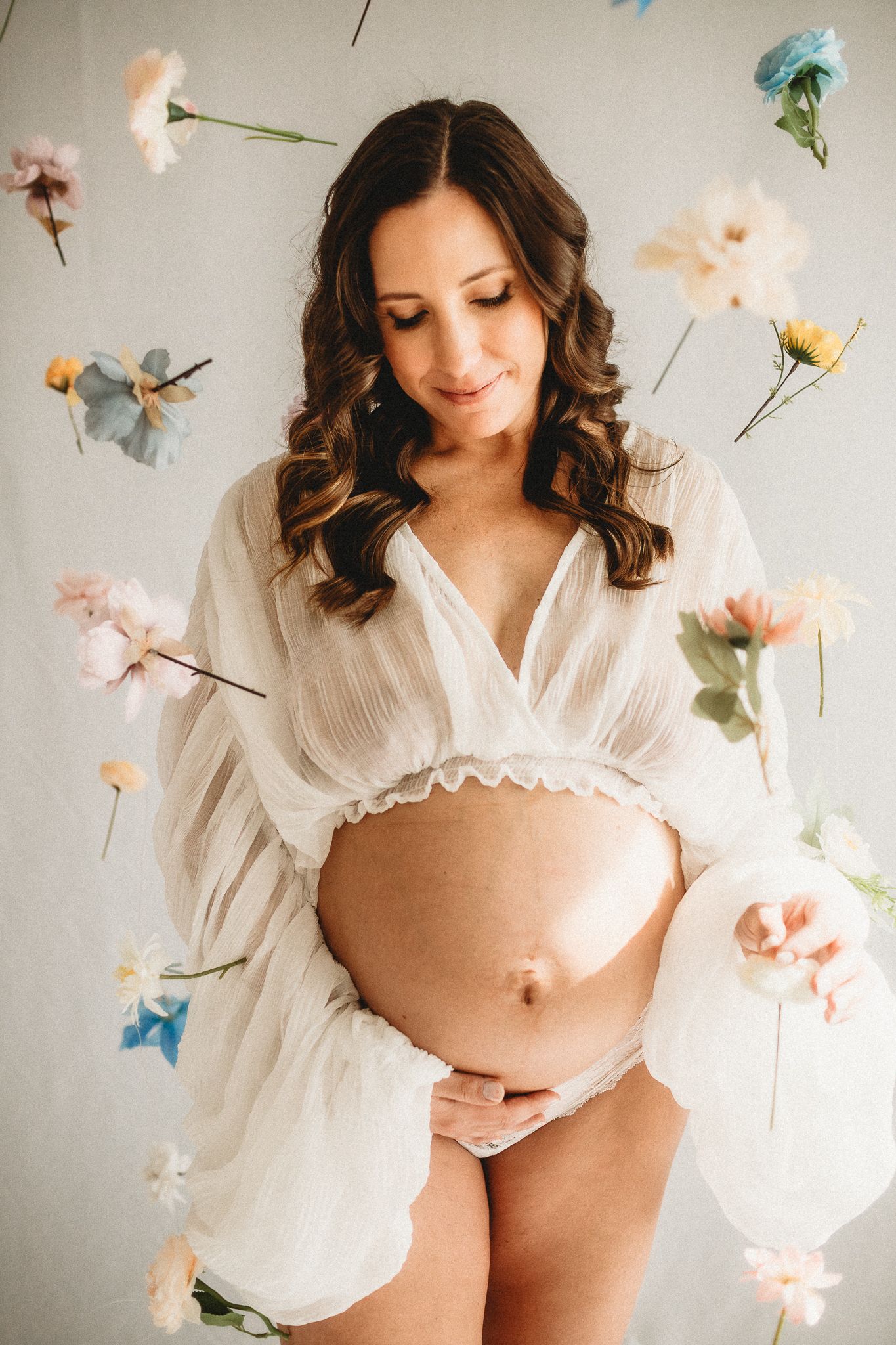 Artistic maternity portrait with floating pastel flowers against white background.