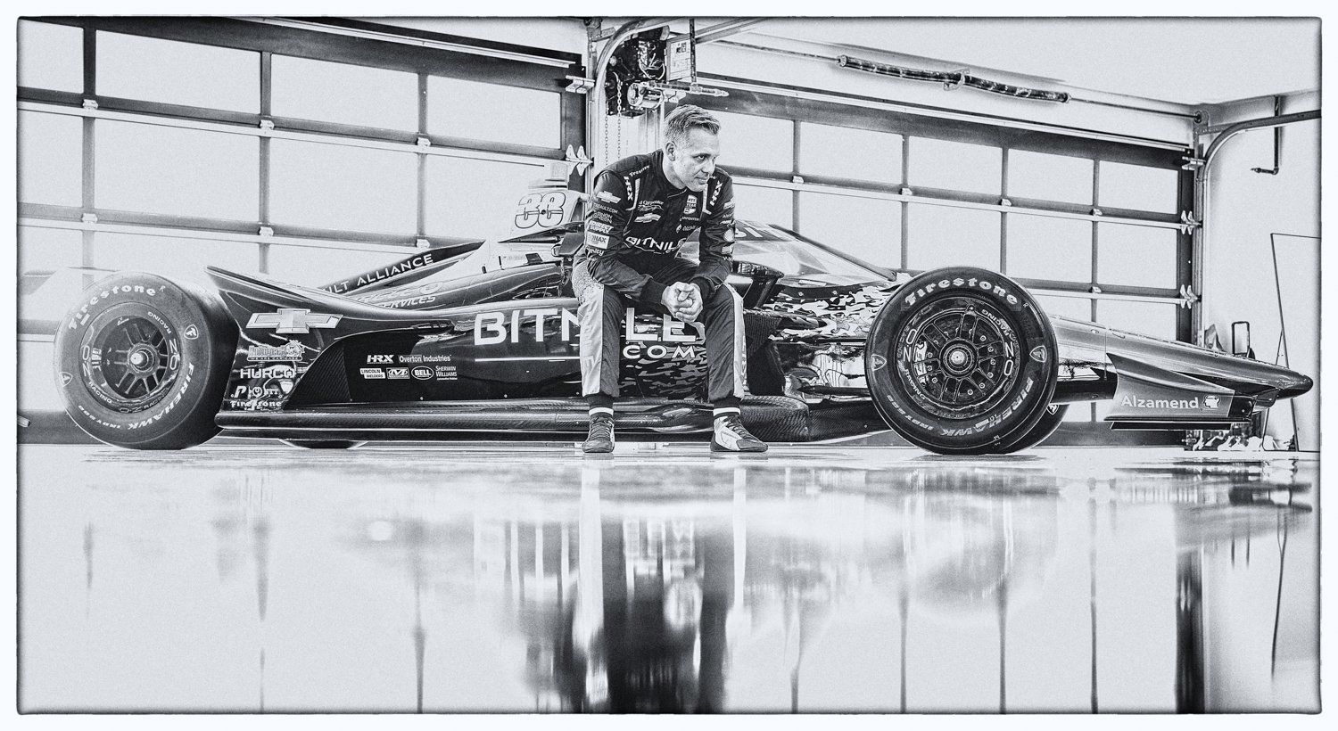 Black and white high contrast photo of a vintage race car in a garage bay with reflective floor.