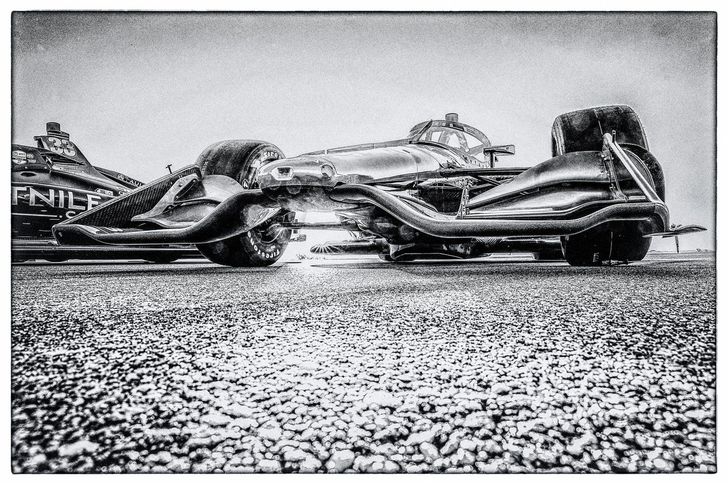Two Indy 500 cars photographed in black and white on asphalt surface.