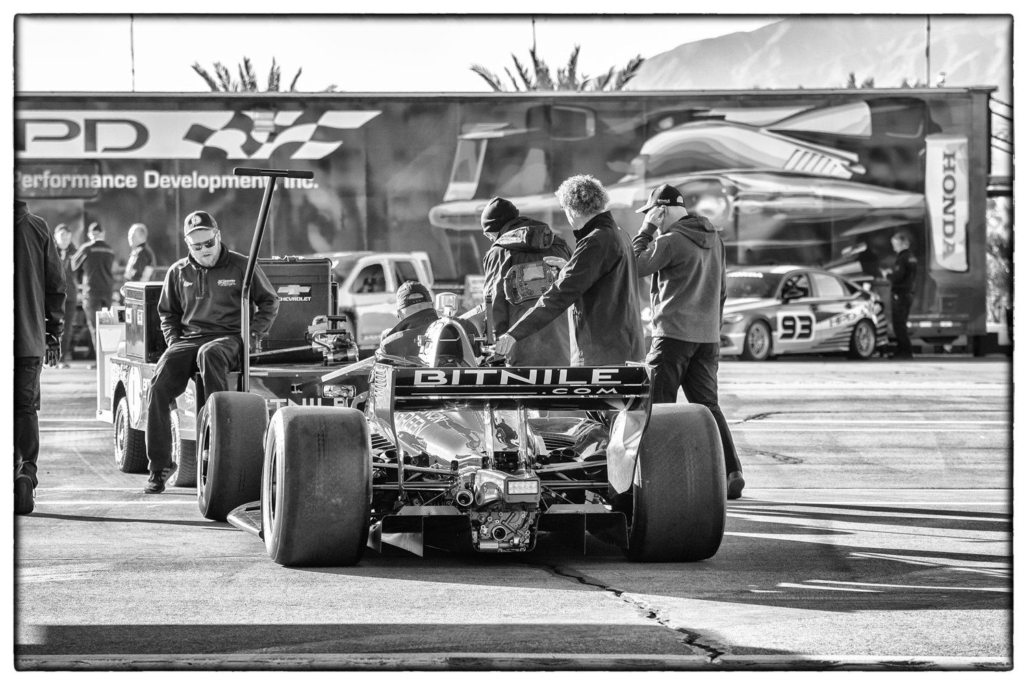 Black and white photo of pit crew working on Formula 1 car during race day.
