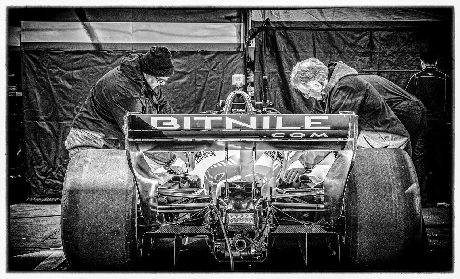 Mechanics working on the rear section of a race car in black and white.