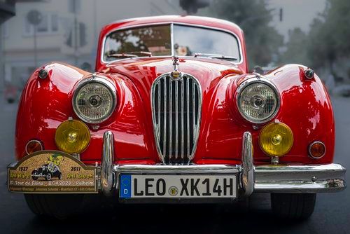 Shiny red classic Jaguar car with chrome grille and yellow fog lights viewed from front.