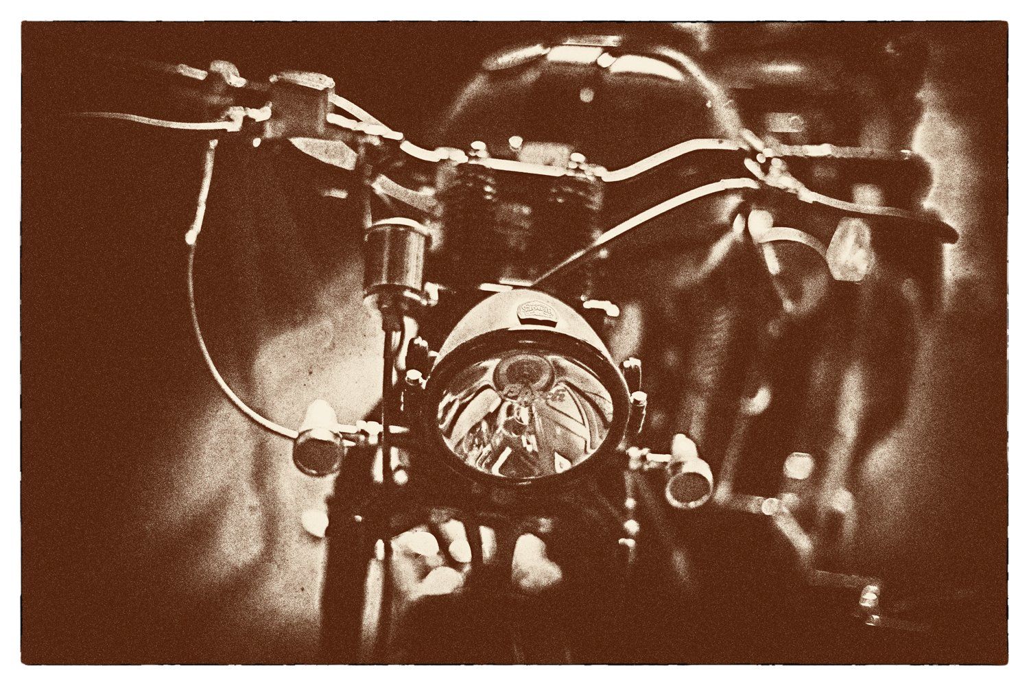 Sepia-toned vintage motorcycle headlight and handlebars in moody lighting.