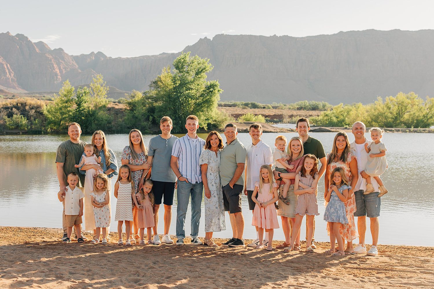 Large family group photo outdoors near a river with mountain backdrop on a sunny day.