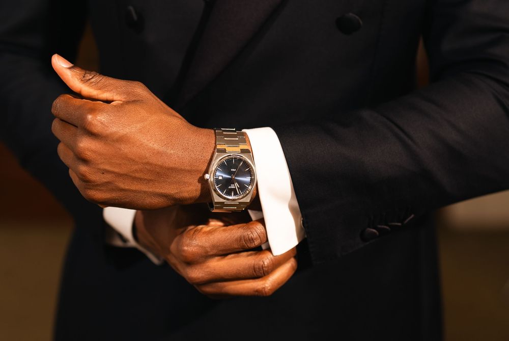 Man in black suit adjusting luxury watch on wrist, showcasing elegant cufflinks and sophisticated style.