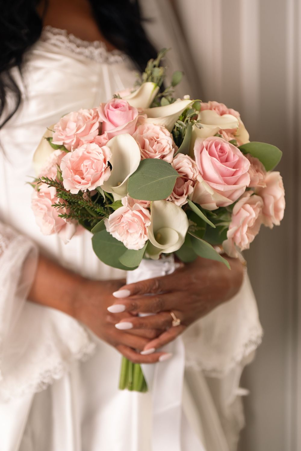 Bride in white gown holding elegant bridal bouquet of pink roses and white calla lilies with eucalyptus greenery.