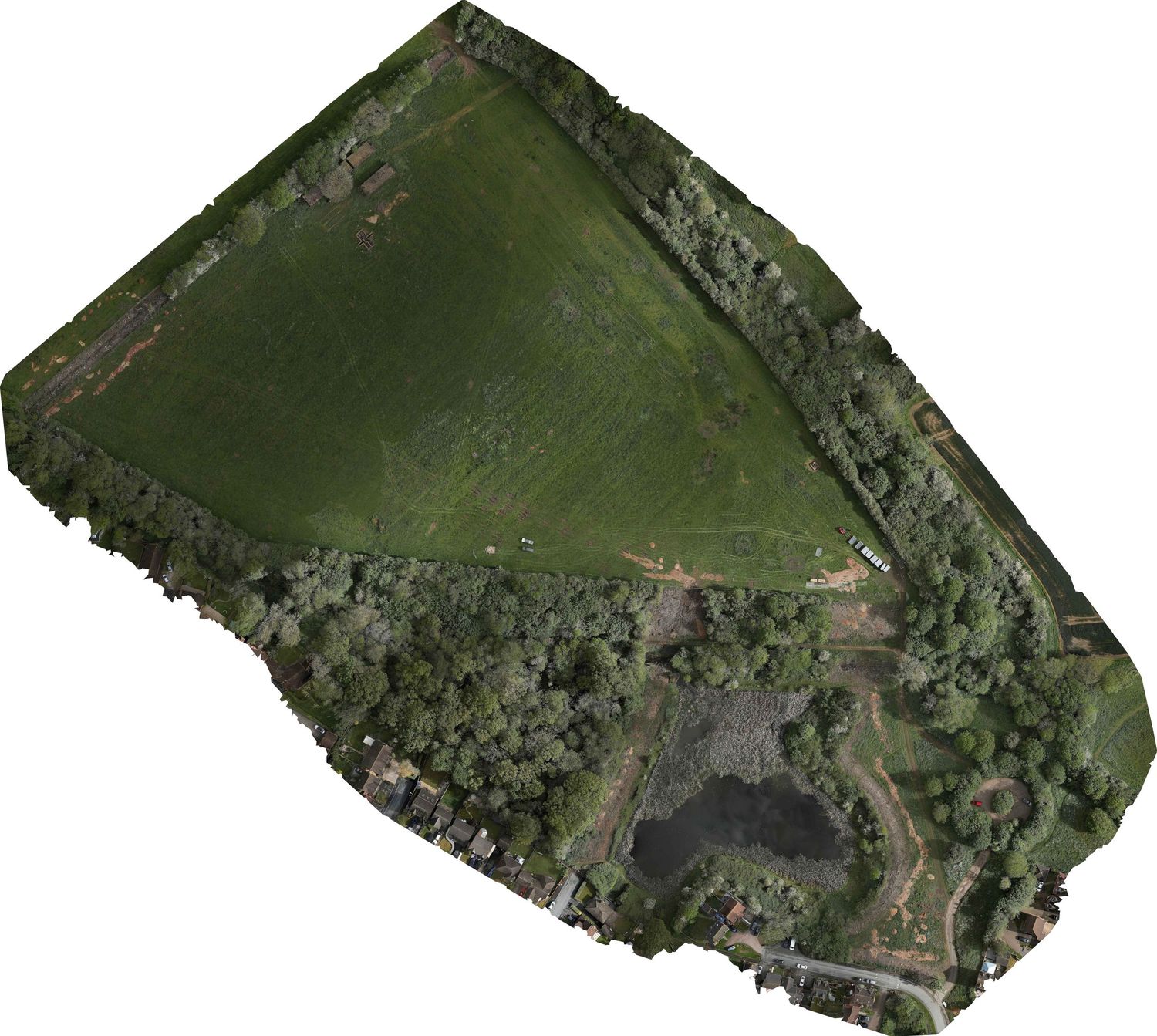 Aerial view of a green agricultural field surrounded by dense woodland and a small pond in a rural landscape.