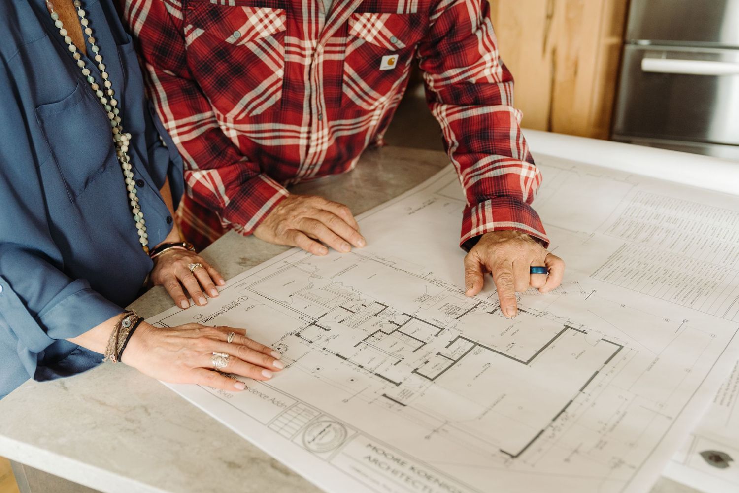 Two people reviewing architectural blueprints on a table, collaborating on a home construction or renovation project.