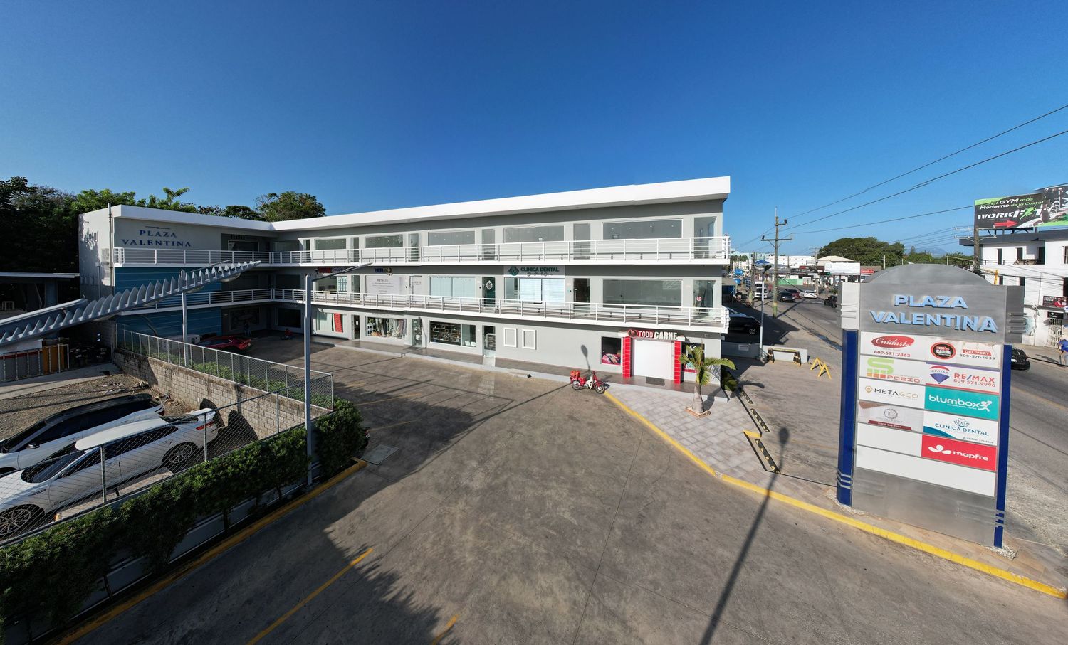 Modern white commercial plaza with retail spaces, parking area and business signage in sunny day.