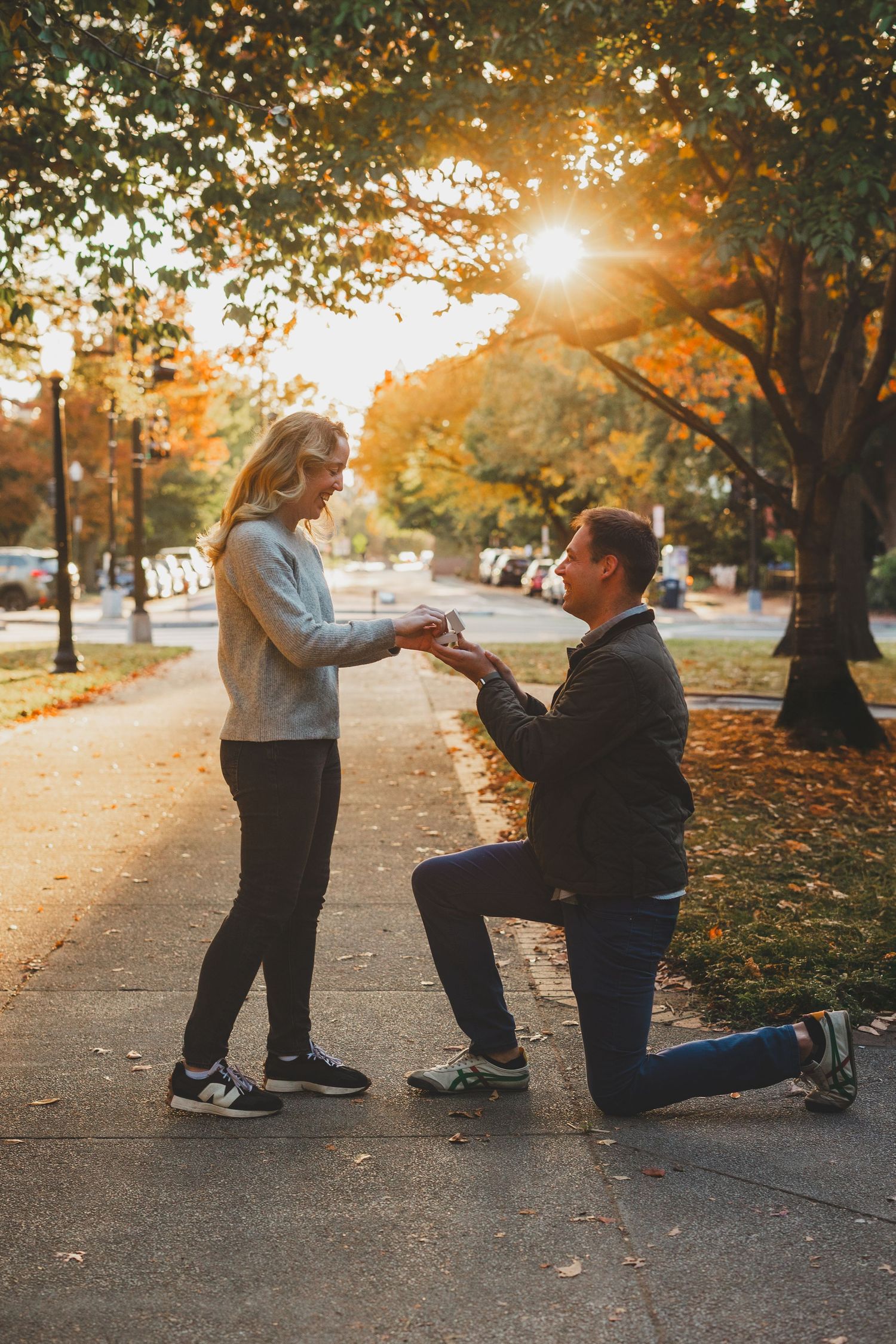 Man proposing on one knee to woman on a tree-lined path during golden hour autumn sunset at the Stanton Park in DC