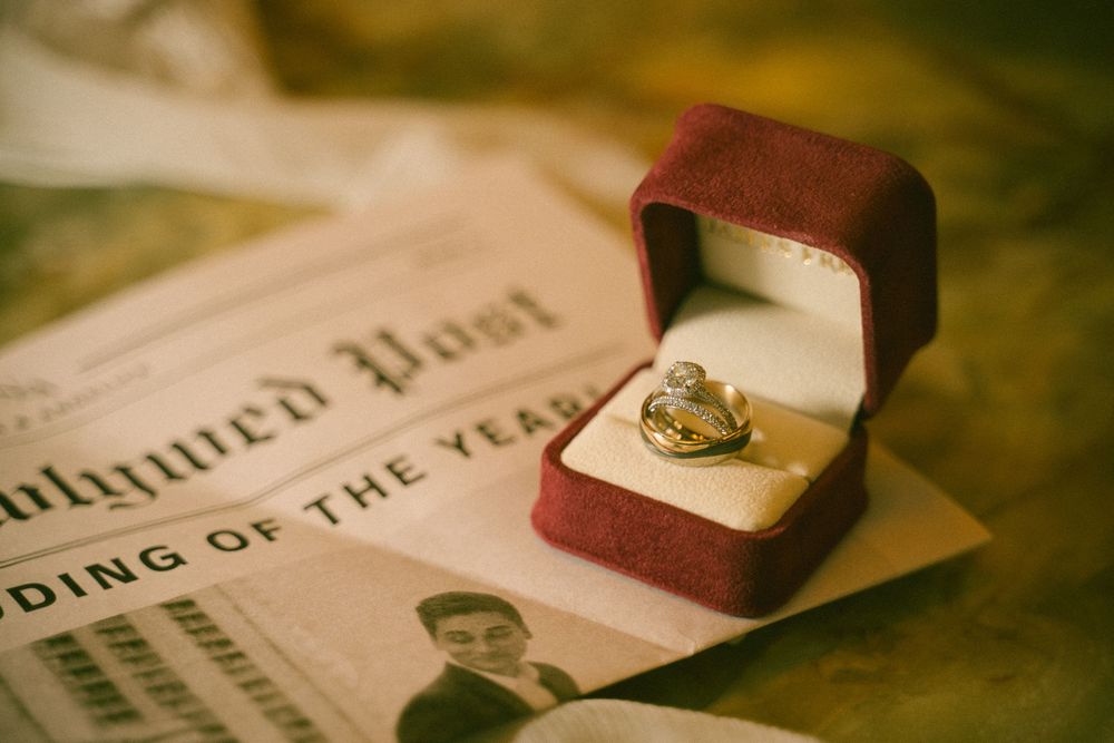 Gold engagement ring in red velvet box displayed on vintage newspaper wedding announcement.