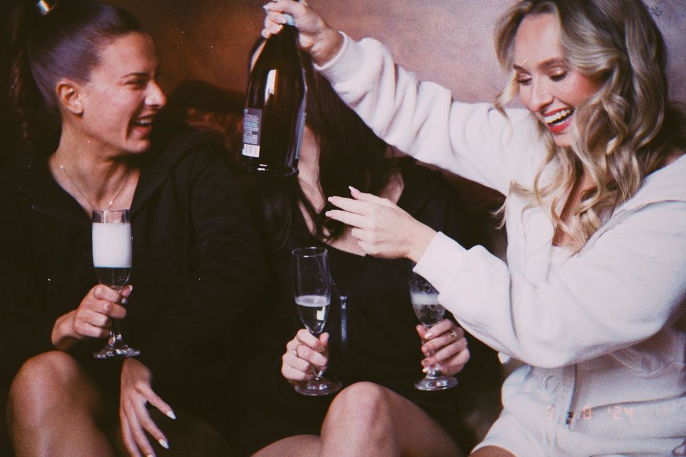 Three women celebrating with champagne bottles and glasses, laughing and having fun at a party.