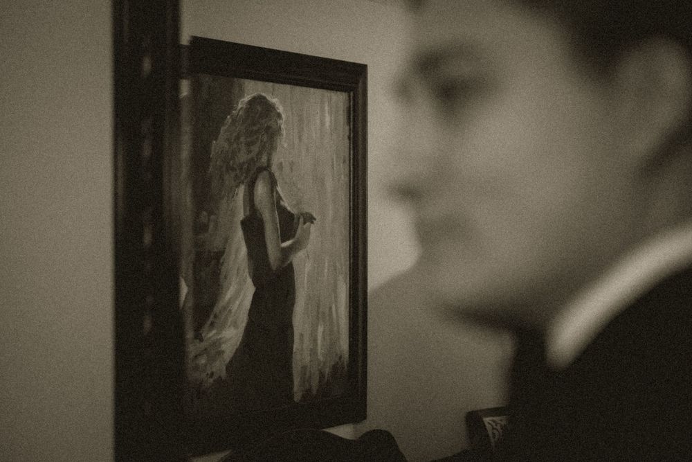 Black and white photo of a man looking at a framed painting of a woman in an elegant red dress.