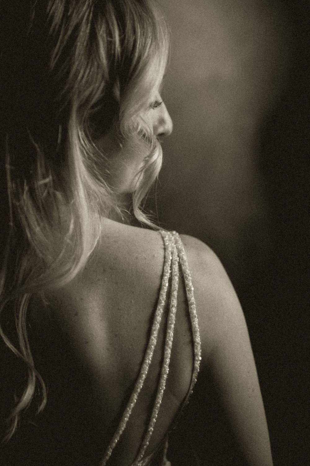 Black and white photo of a woman in an elegant backless gown with strappy details, her blonde hair cascading over her shoulder.