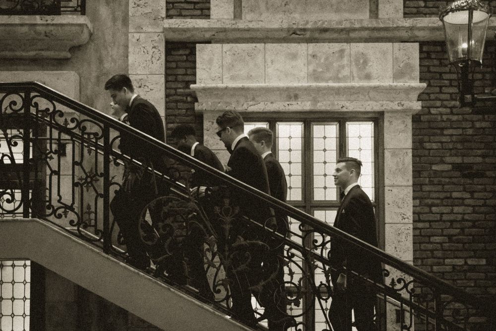 Men in formal suits ascending an ornate iron staircase outside a brick building in a vintage black and white photo.