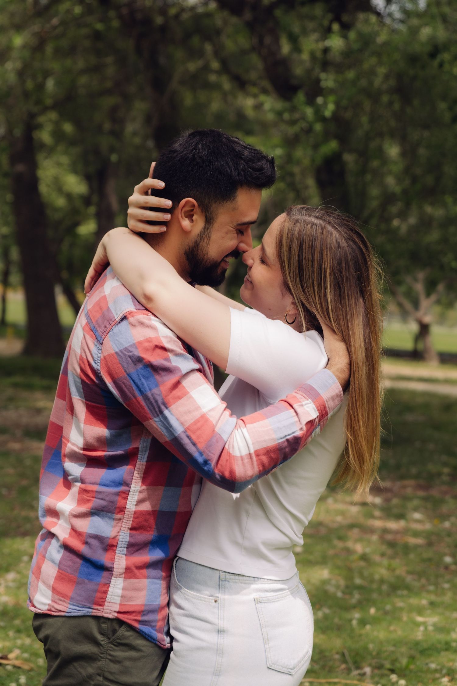Loving couple embracing face-to-face with arms around each other in a green park surrounded by trees.