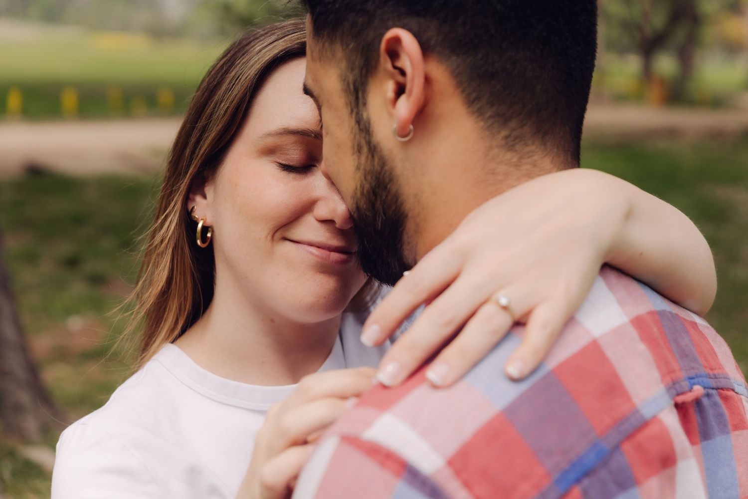Close-up of a couple sharing an intimate moment, woman smiling with eyes closed while embracing man in plaid shirt.