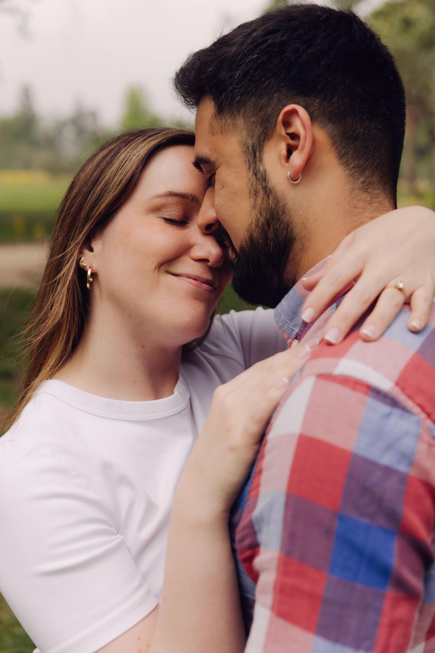 Happy couple with eyes closed share an intimate forehead-to-forehead moment in a park.