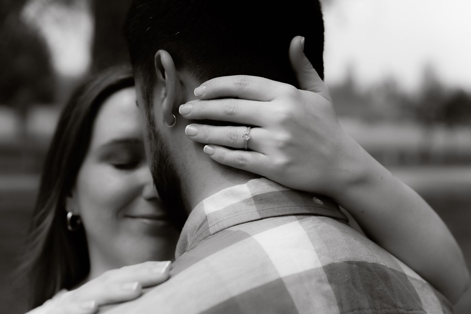 Black and white close-up of woman with engagement ring embracing her partner tenderly.