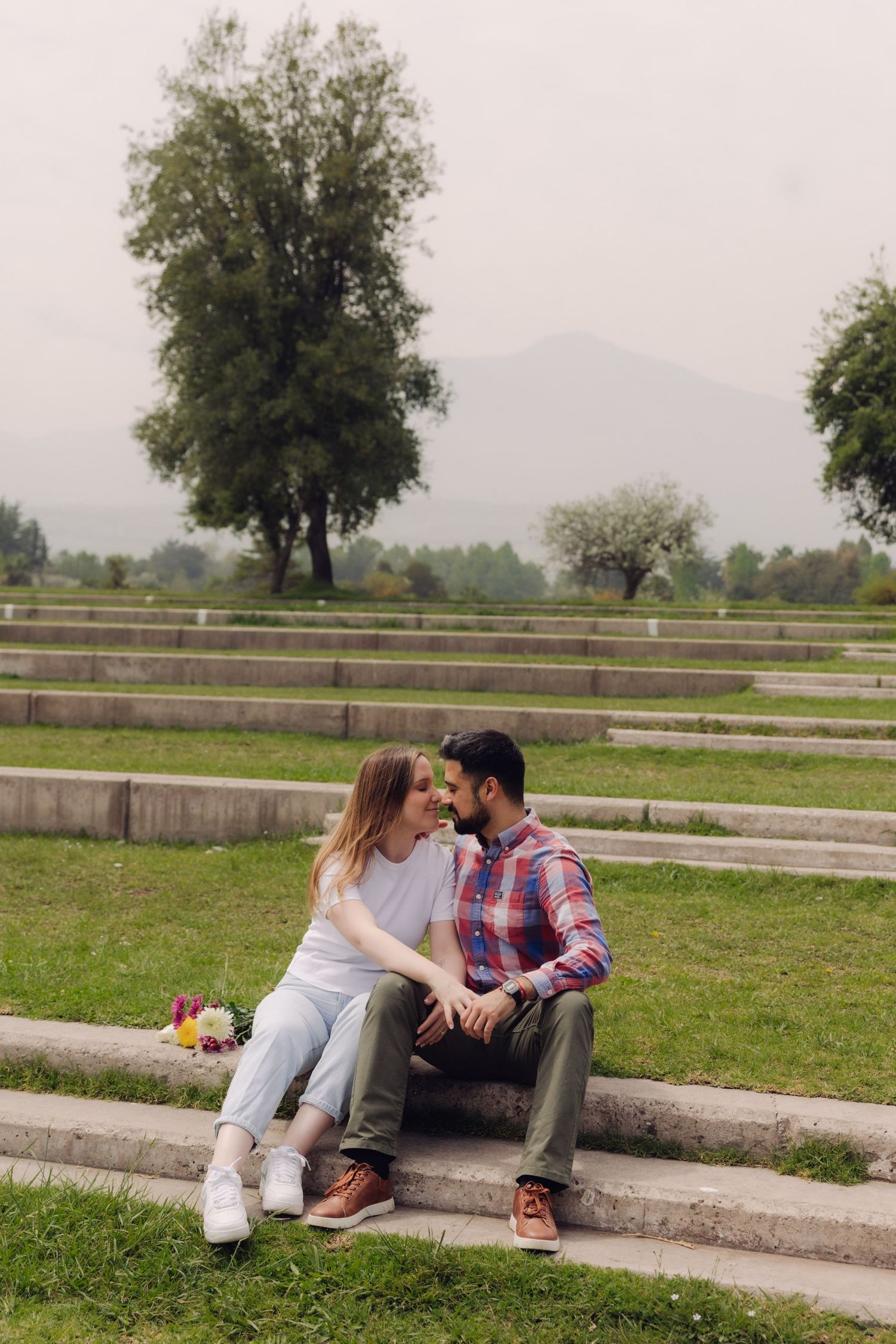 Couple sitting close on stone steps in a scenic park with mountains in the background.