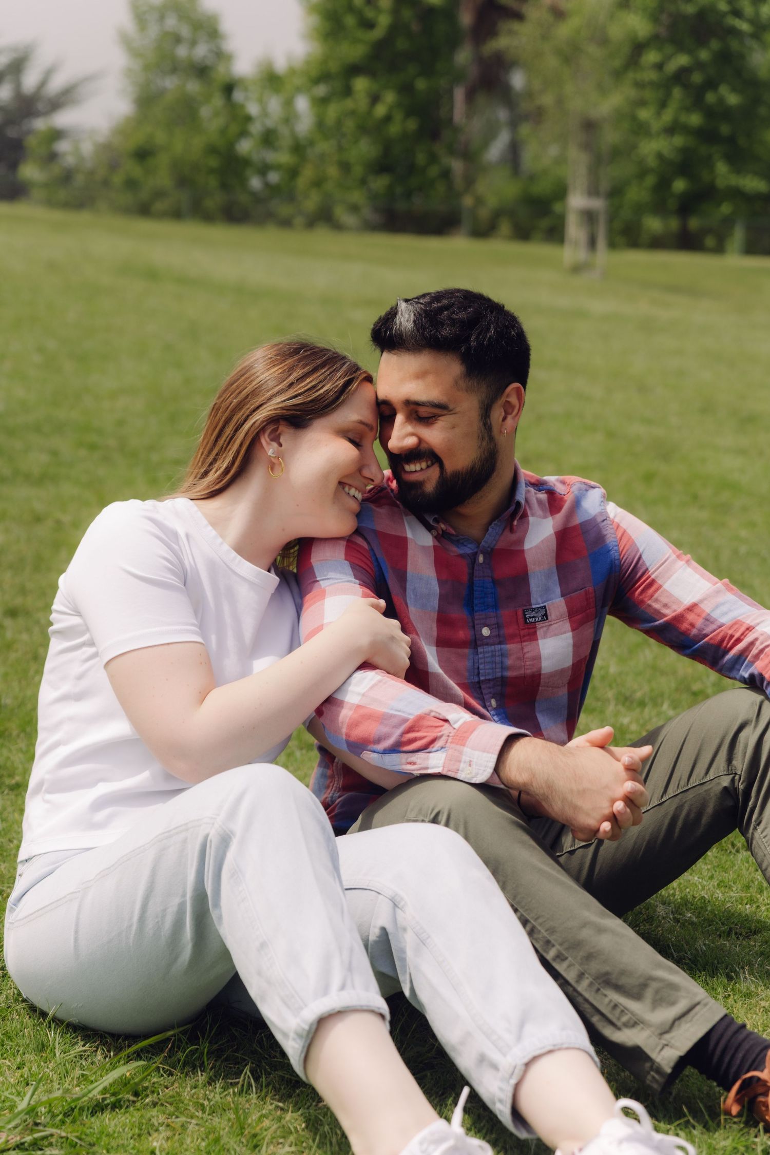 Happy interracial couple sitting together on grass in a park, smiling and holding hands.