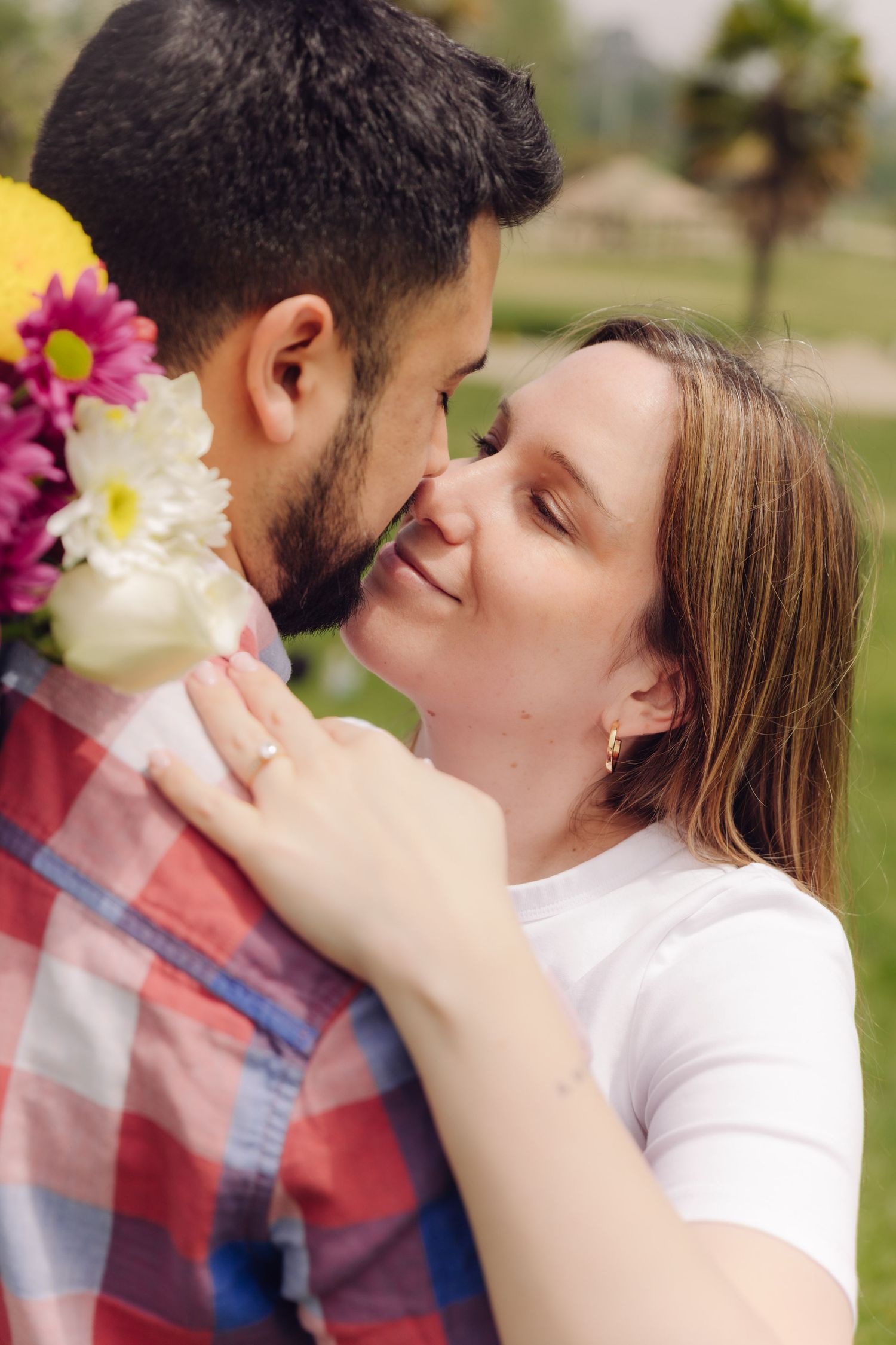 Romantic couple nearly kissing outdoors, woman holding colorful flower bouquet against mans chest.