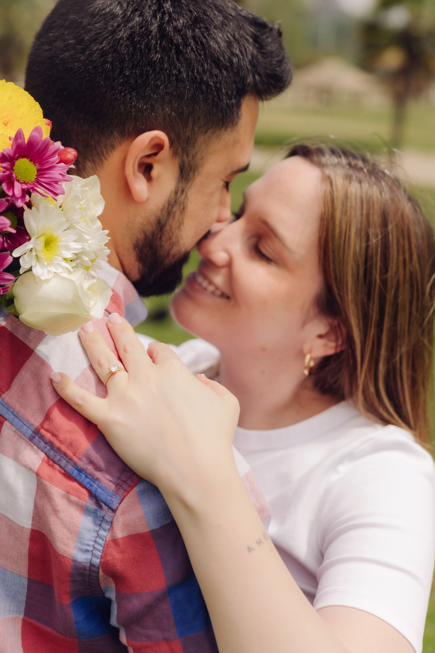 Joyful couple sharing an intimate moment outdoors, woman smiling while holding a colorful bouquet.