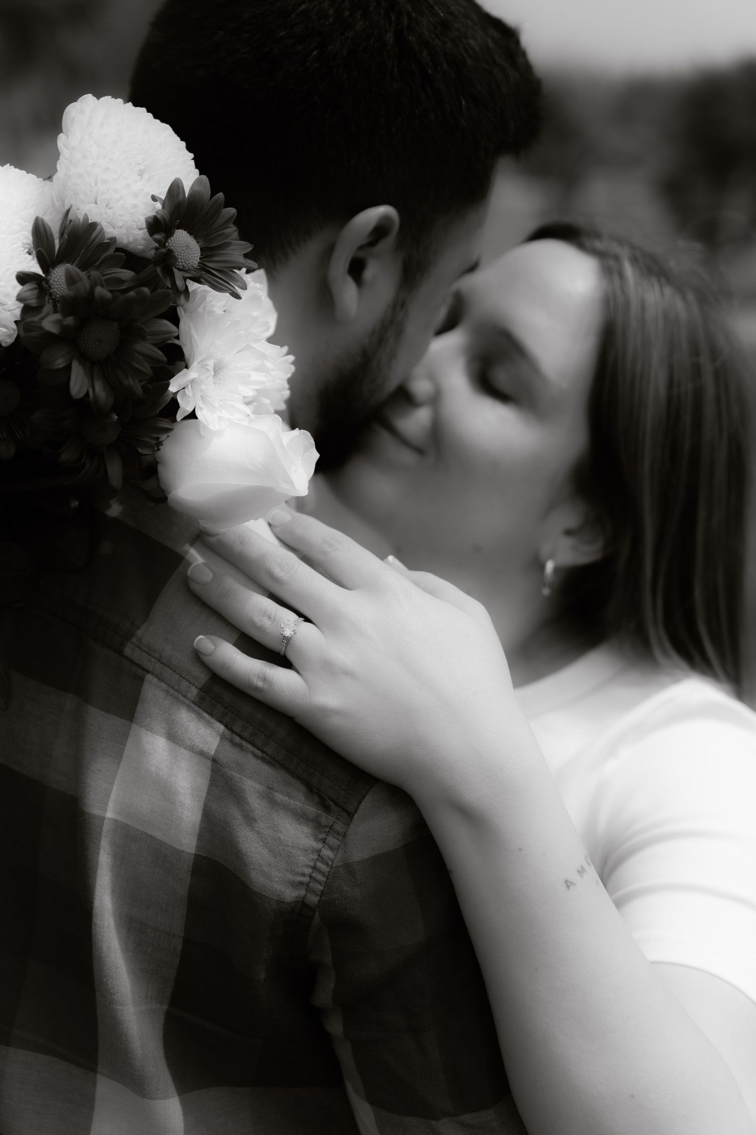 Black and white photo of couple sharing a tender kiss, woman holding a bouquet of flowers.