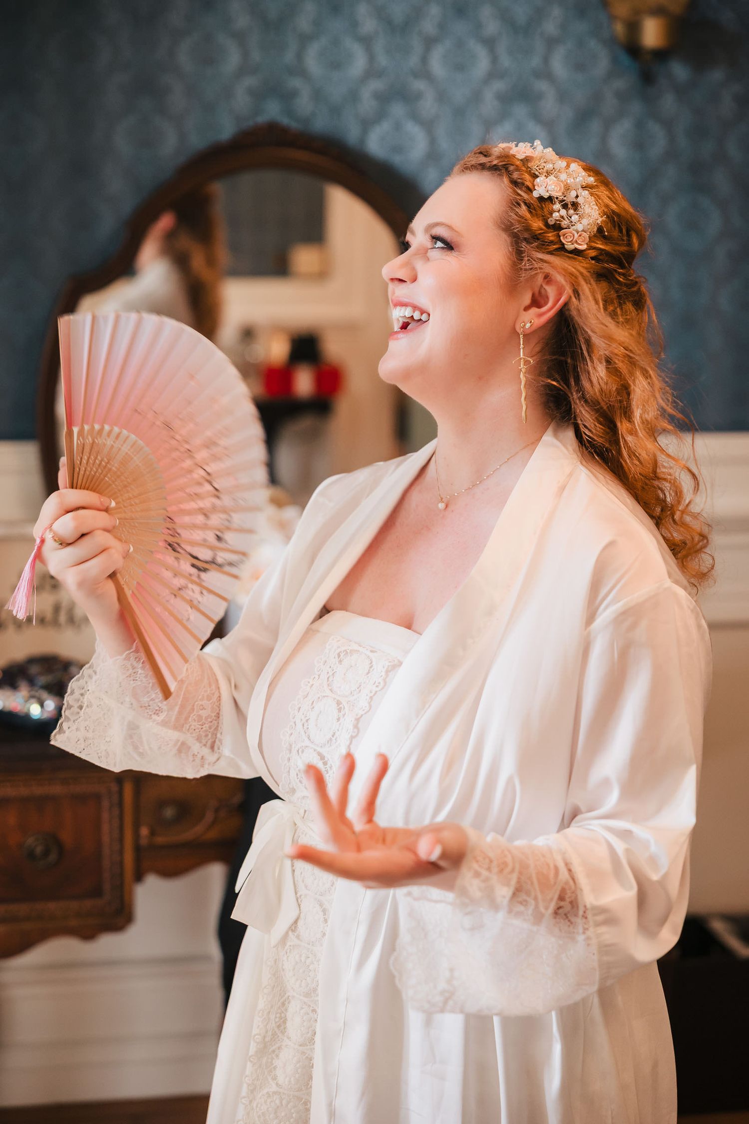 Bride laughing and fanning herself in her robe at the start of wedding day preparations at Searles Castle.