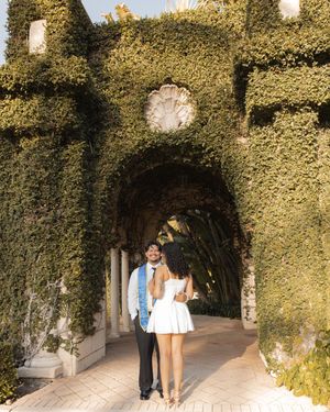 Couple posing under an ivy-covered stone archway at an elegant garden venue on a sunny day.