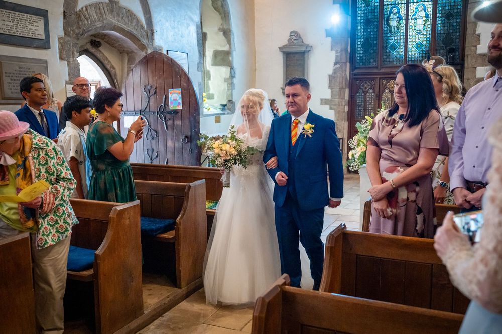 Bride and groom walking down church aisle during wedding ceremony, surrounded by guests in wooden pews.