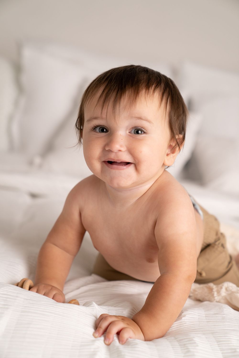 Adorable smiling baby lying on white bedding, looking up with bright eyes and a joyful expression.