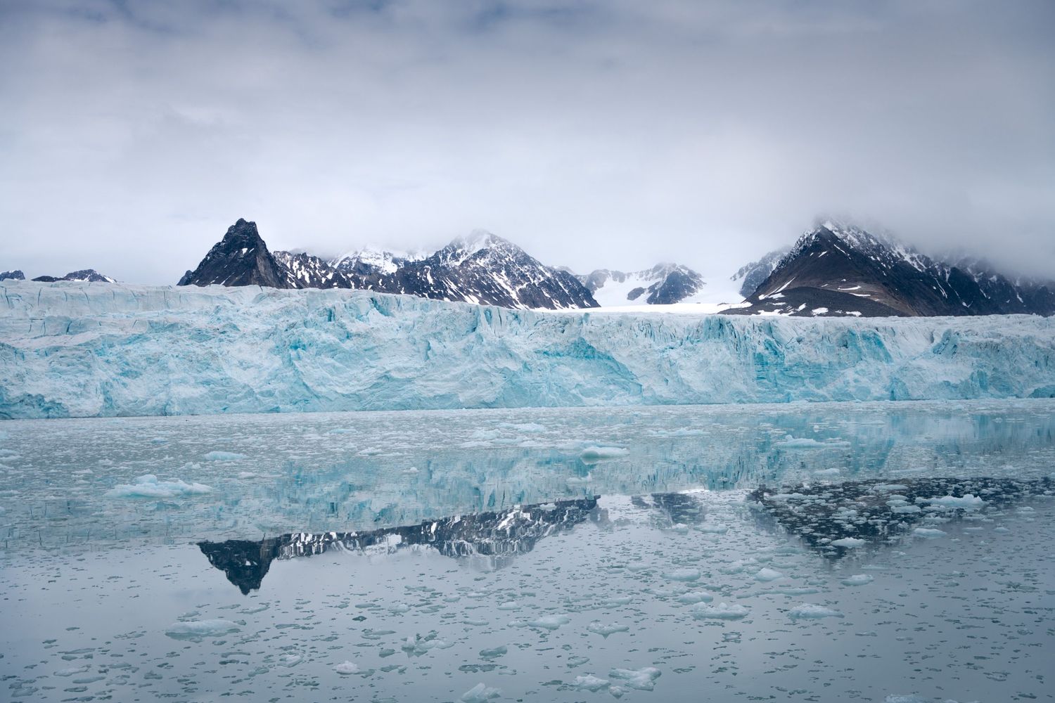Longue muraille de glace et montagnes reflétées dans un fjord lisse du Svalbard