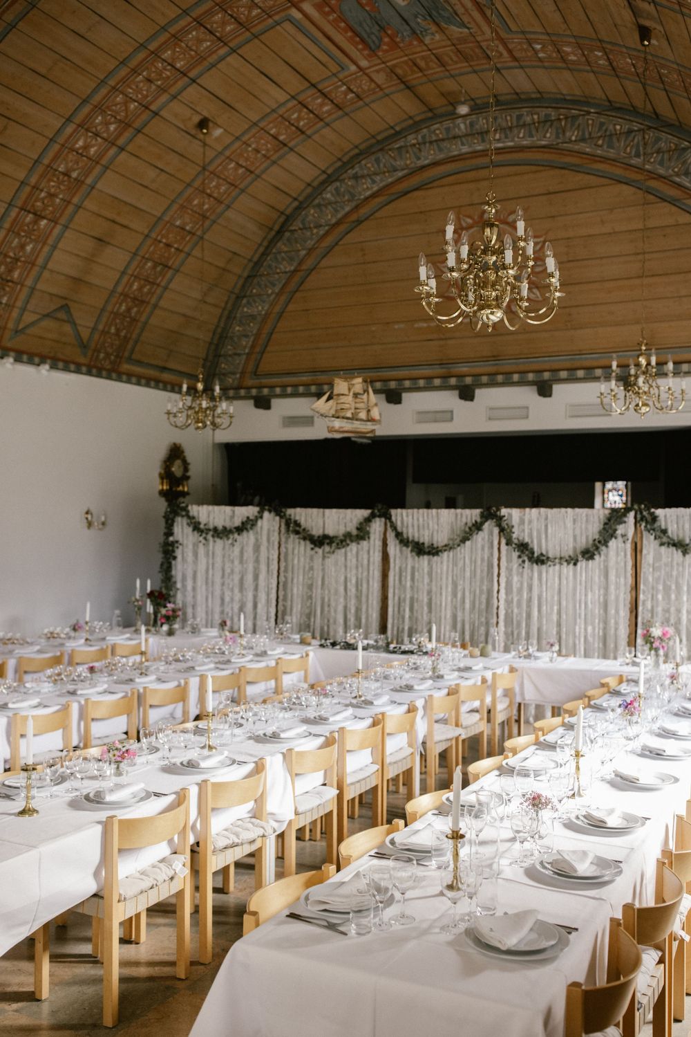 Elegant wedding reception hall with long tables, white linens, chandeliers, and barrel ceiling.