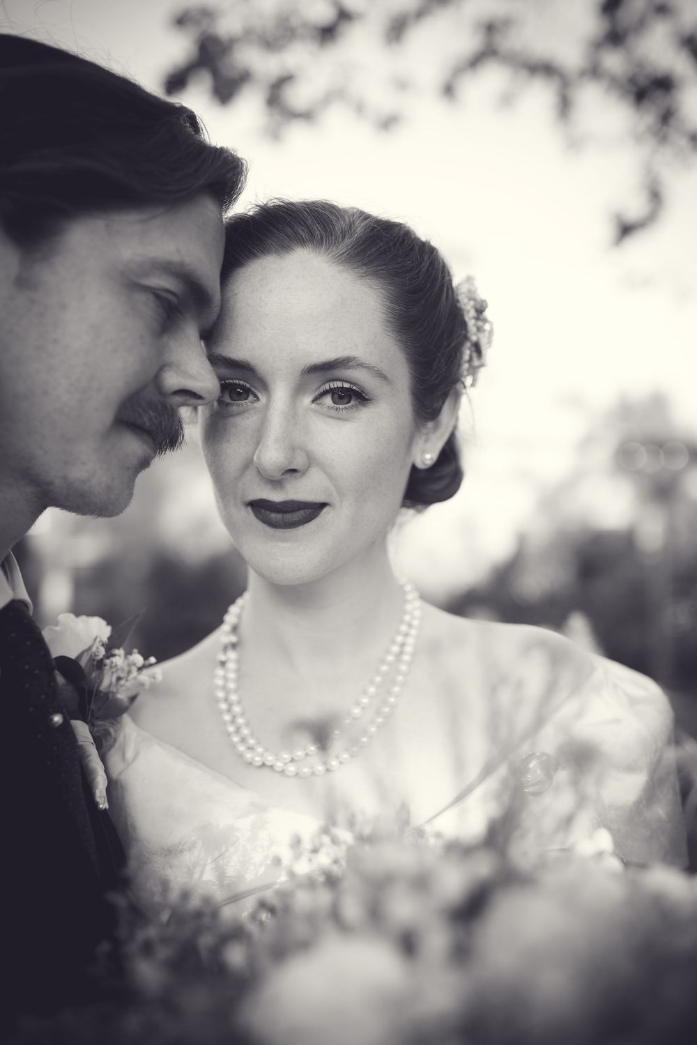 Black and white wedding portrait of bride wearing pearl necklace and groom in bow tie sharing an intimate moment.
