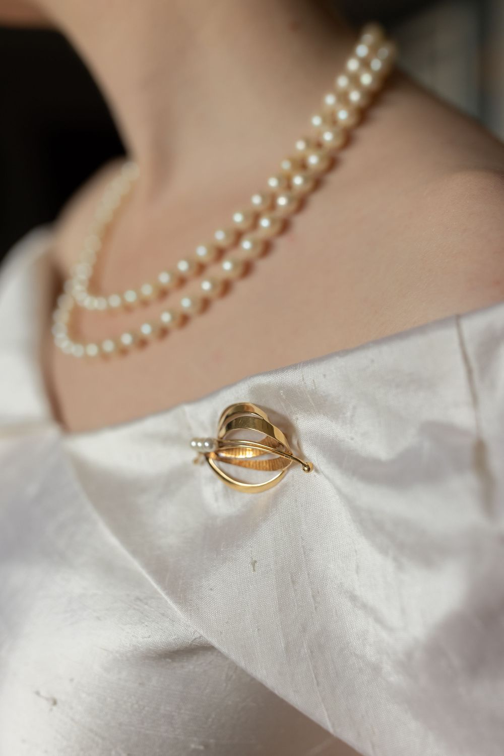 Close-up of gold brooch and double strand pearl necklace on white wedding dress.Elegant