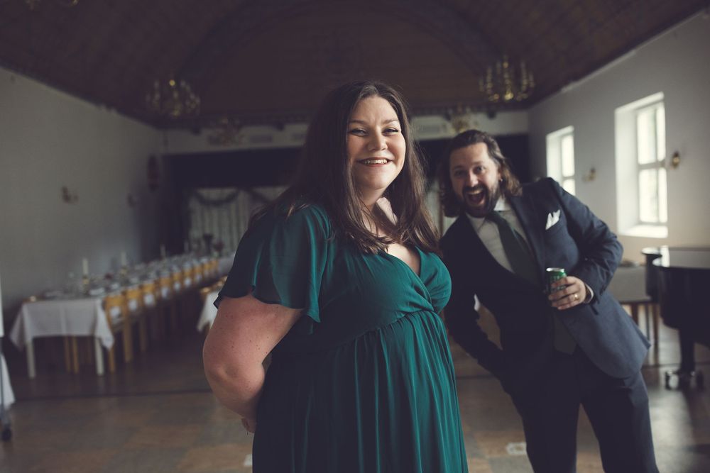 Joyful woman in emerald green dress laughing as bearded man in suit poses playfully behind her.