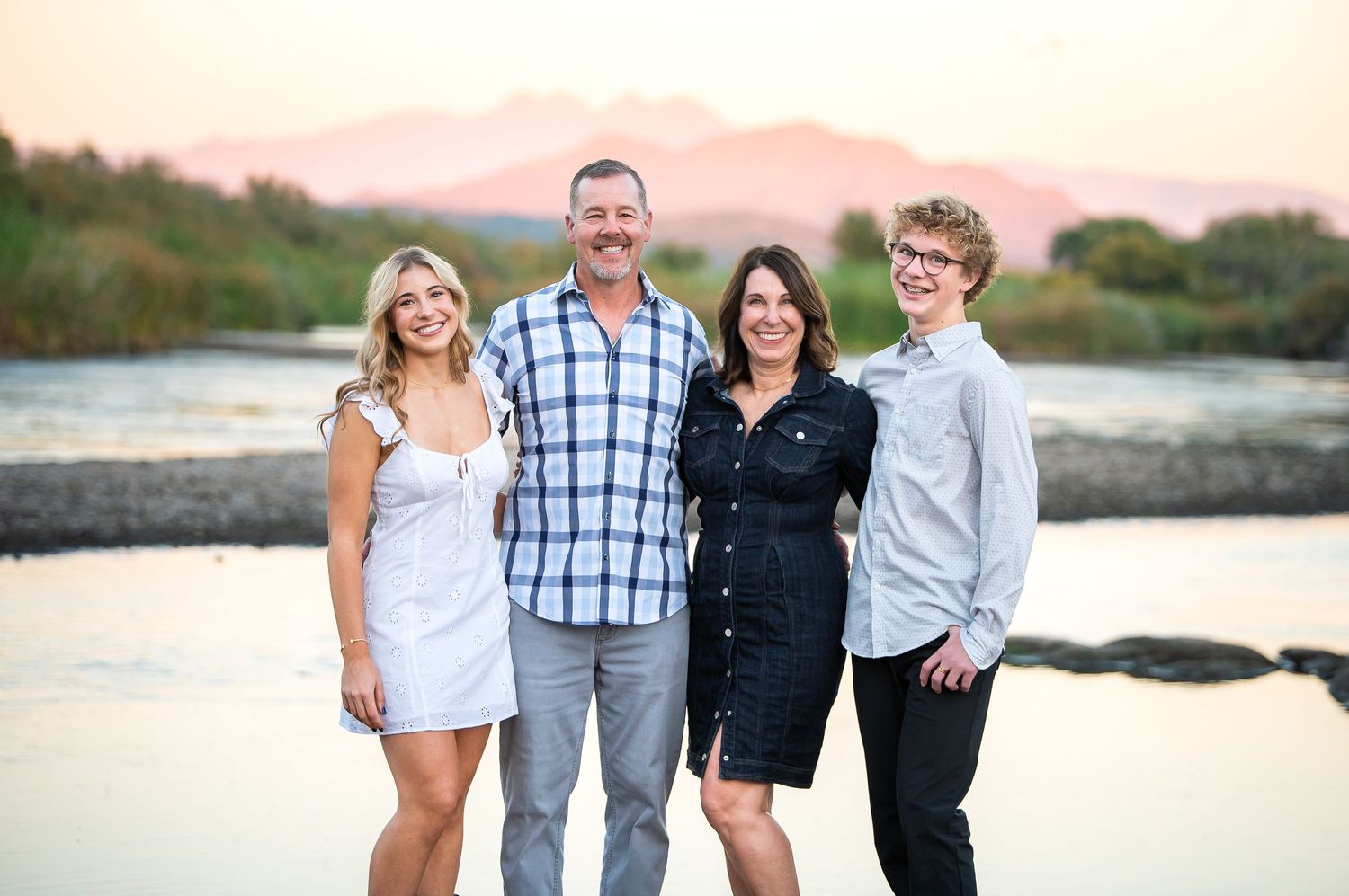 Family of four pose together, smiling and laughing, at golden hour in front of the Salt River during their Arizona family vacation session.
