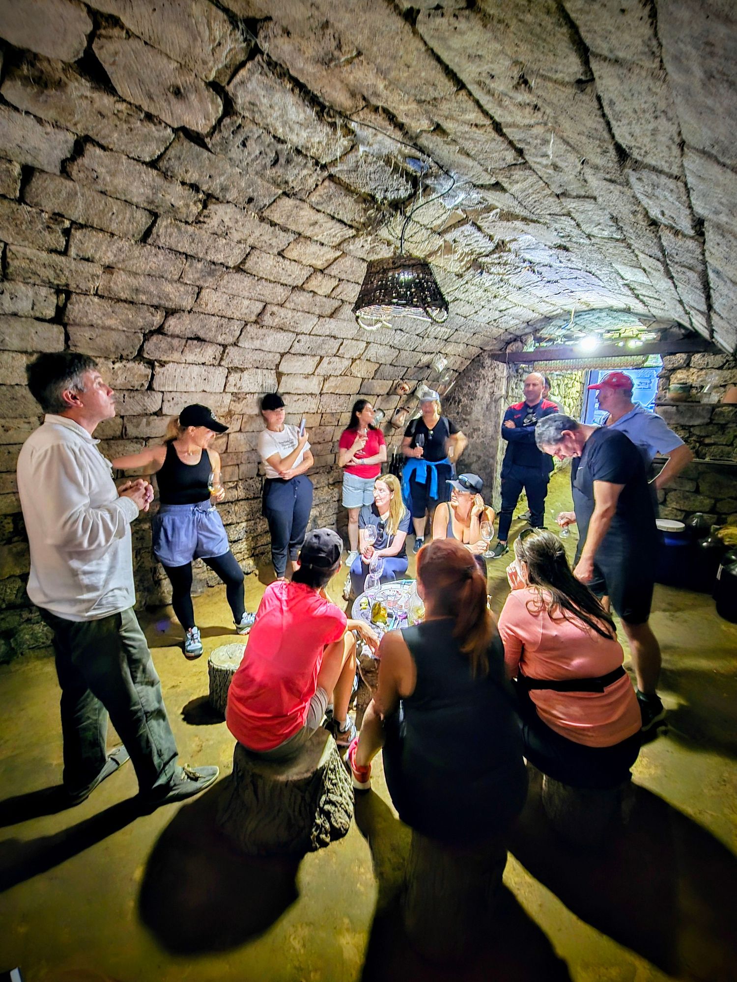 Tour group gathered inside an ancient stone cellar with arched ceiling during a historical underground tour.