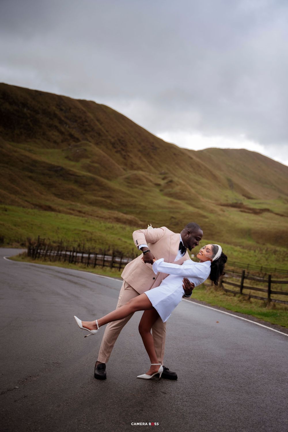 Couple sharing a romantic dip pose on a road with green hills backdrop on their wedding day.