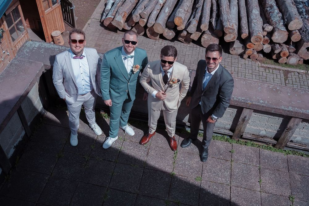 Four people in formal attire stand together on a brick walkway near a pile of logs.
