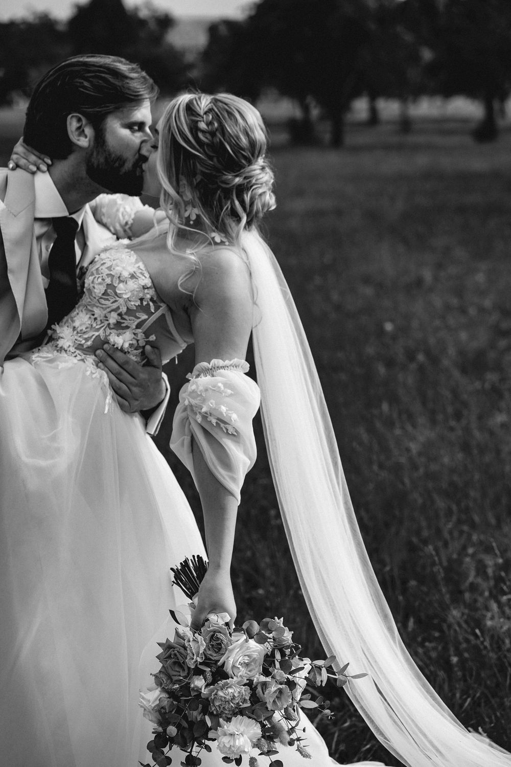 A romantic black and white wedding photo series showing intimate moments between newlyweds in an outdoor field setting.