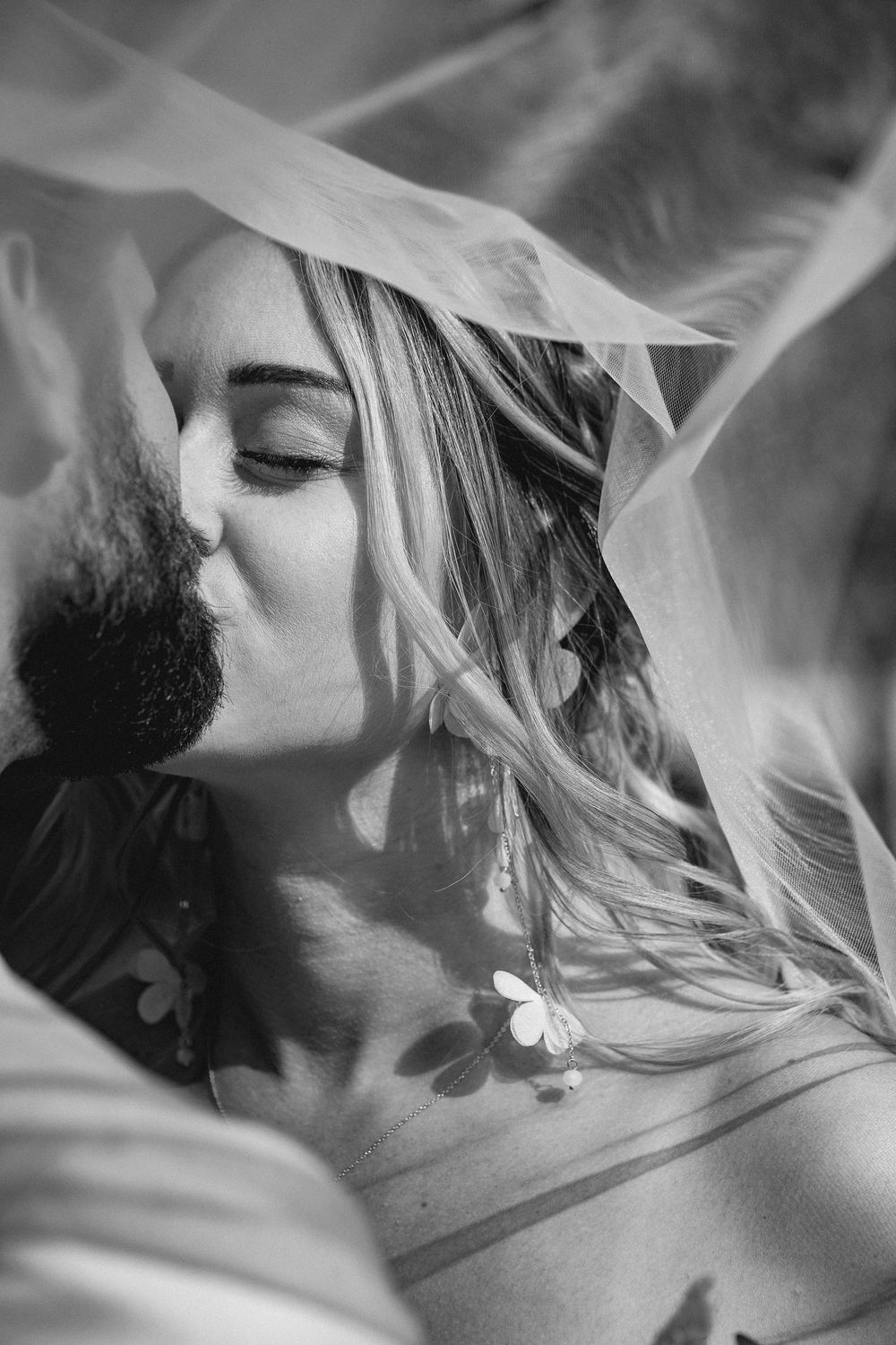 Black and white romantic portrait through delicate veil fabric showing intimate tender moment.