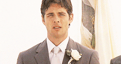 Handsome groom in gray suit with white boutonniere at wedding ceremony, looking emotional and dapper.