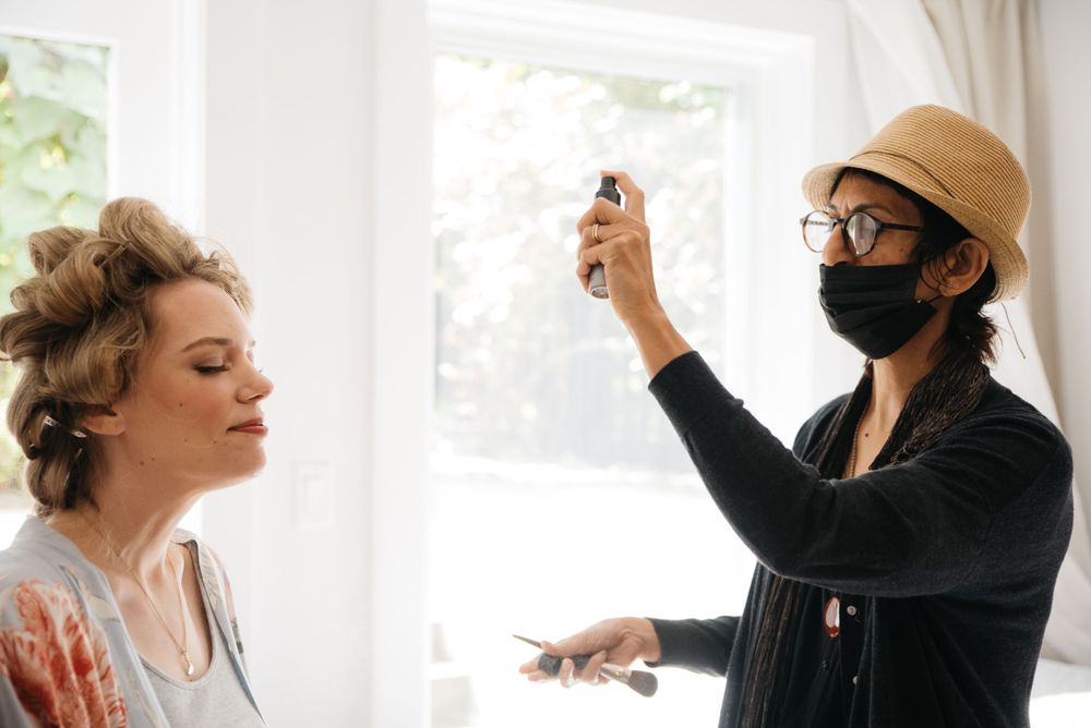 Hair and makeup preparation with stylist spraying product during wedding preparations.
