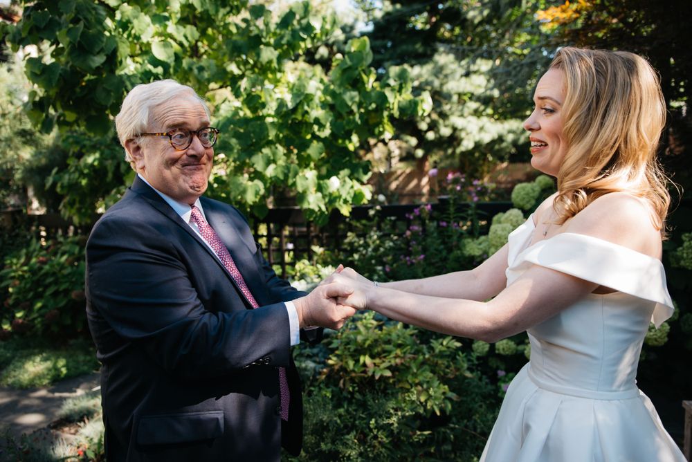 A joyful moment shared between two people dancing in a garden setting on a sunny day.