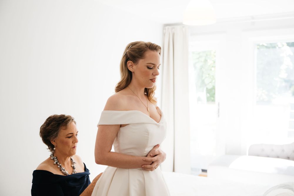 Elegant wedding dress preparation moment in bright sunlit room.