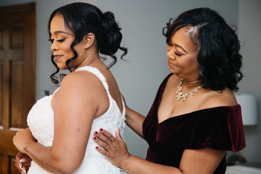 A touching moment during wedding preparations as final dress adjustments are made.