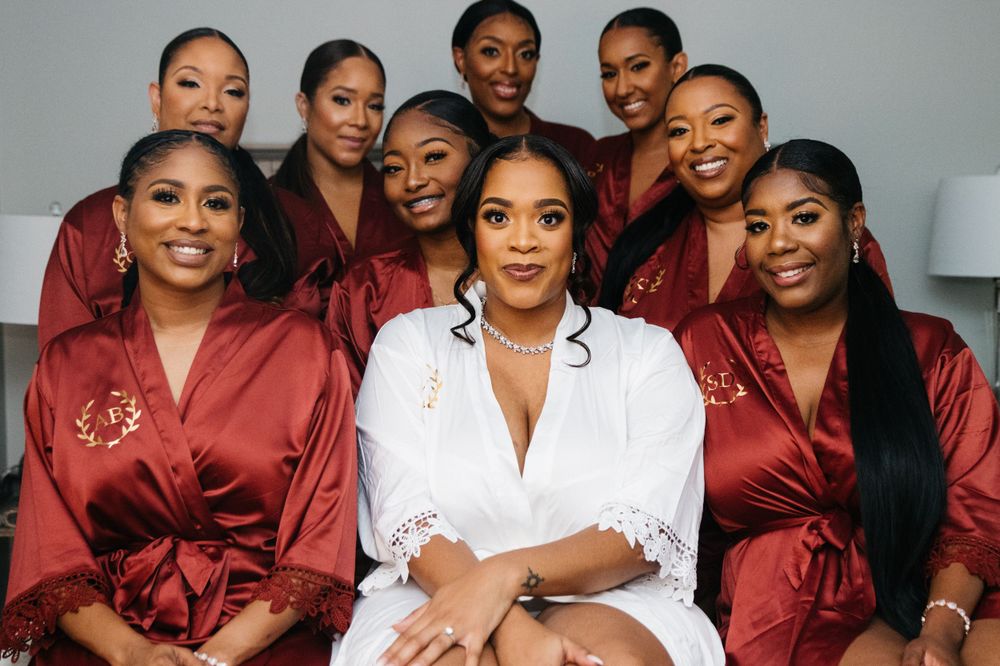 Wedding party poses together with bridesmaids in burgundy satin robes surrounding a central figure in white.