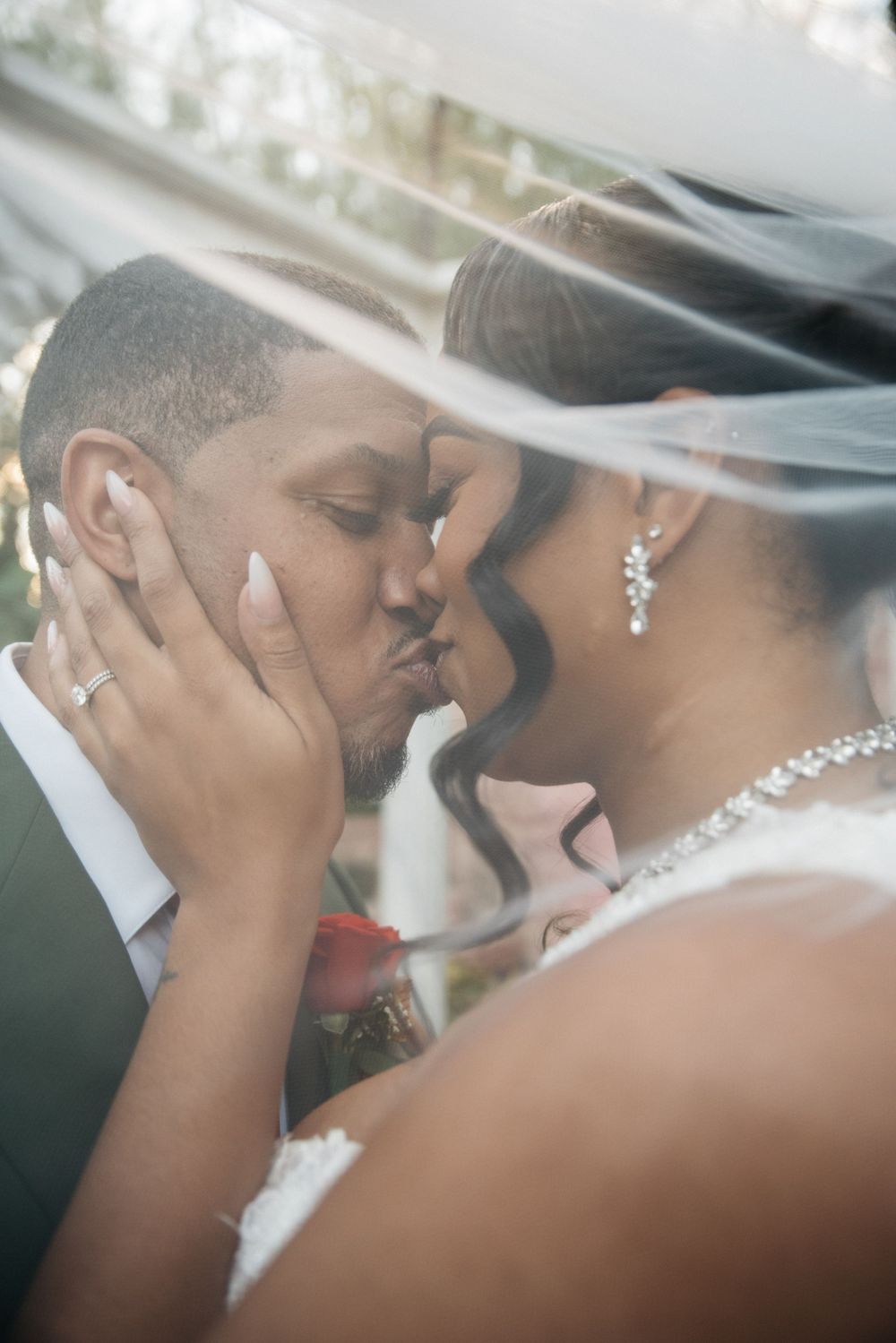 Romantic moment captured under wedding veil with sparkly jewelry and formal attire.